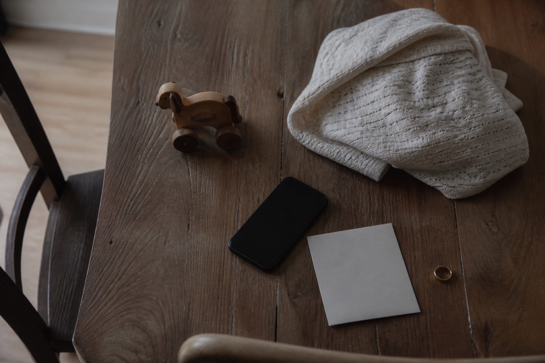 A wooden table with a phone, a folded cloth, a ring and a blank note on it