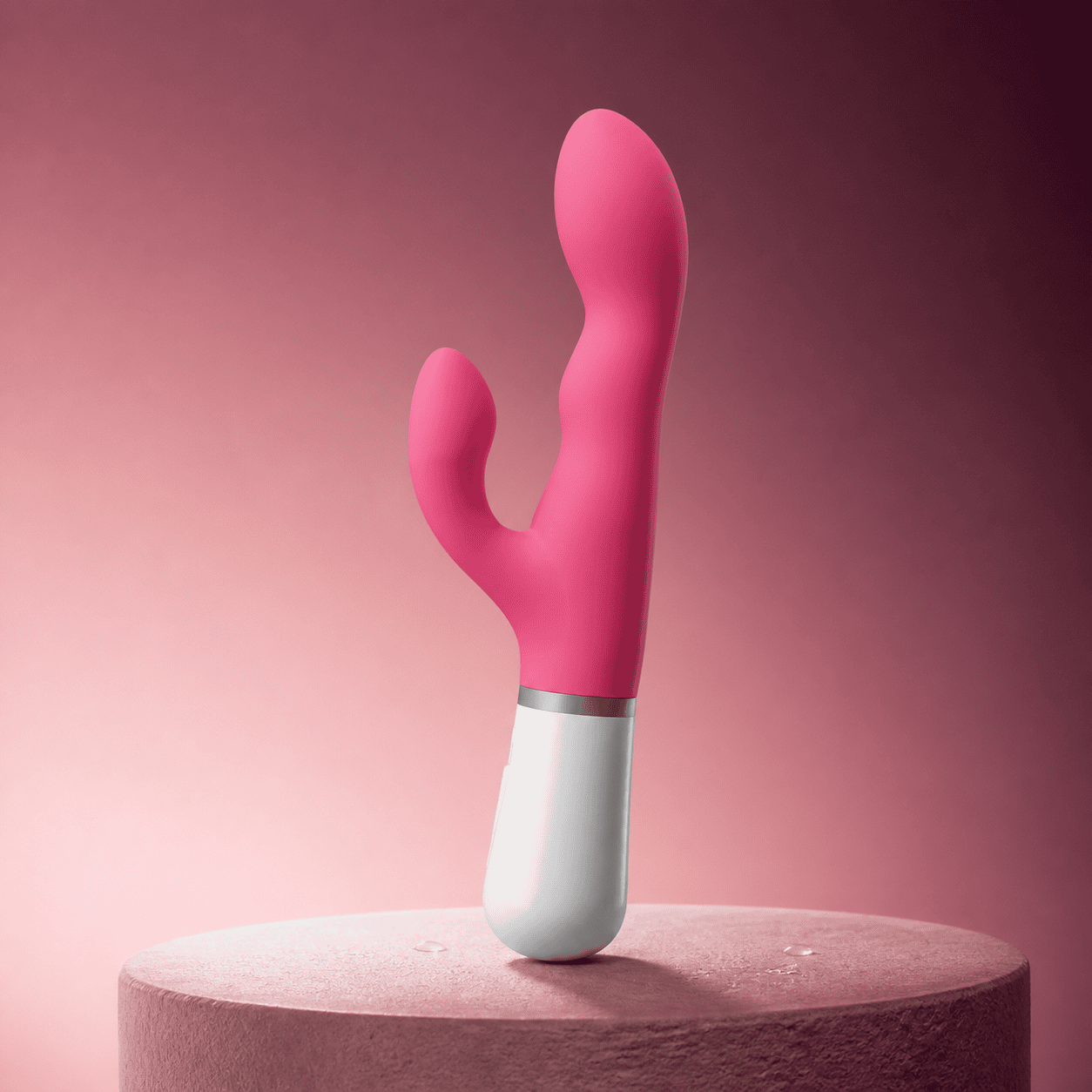 Lovense Nora curved dual-stimulation rabbit vibrator on a dry pedestal with light surface droplets